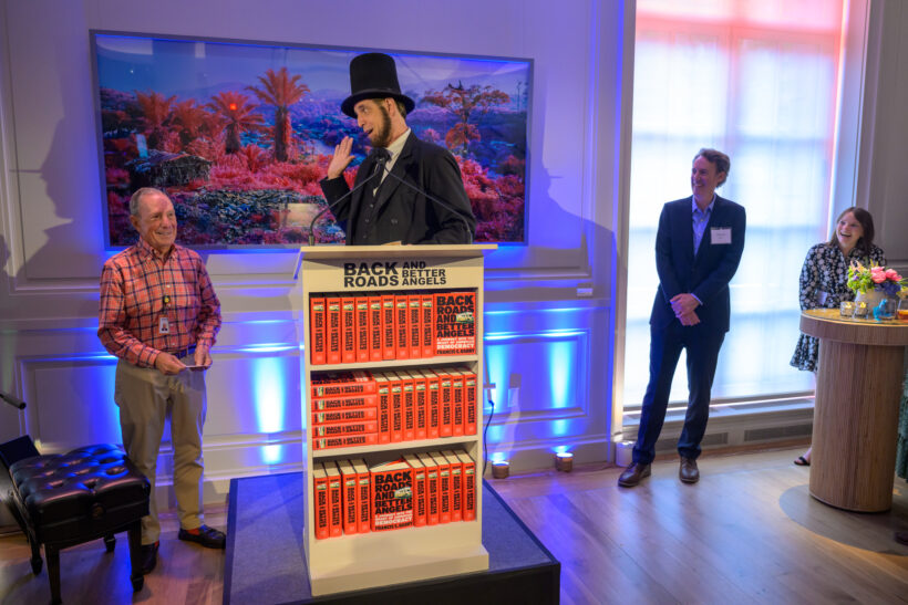 Man in top hat speaking at podium event.