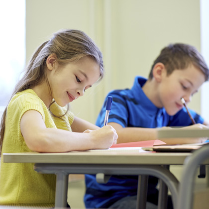 Children writing at desks in classroom.